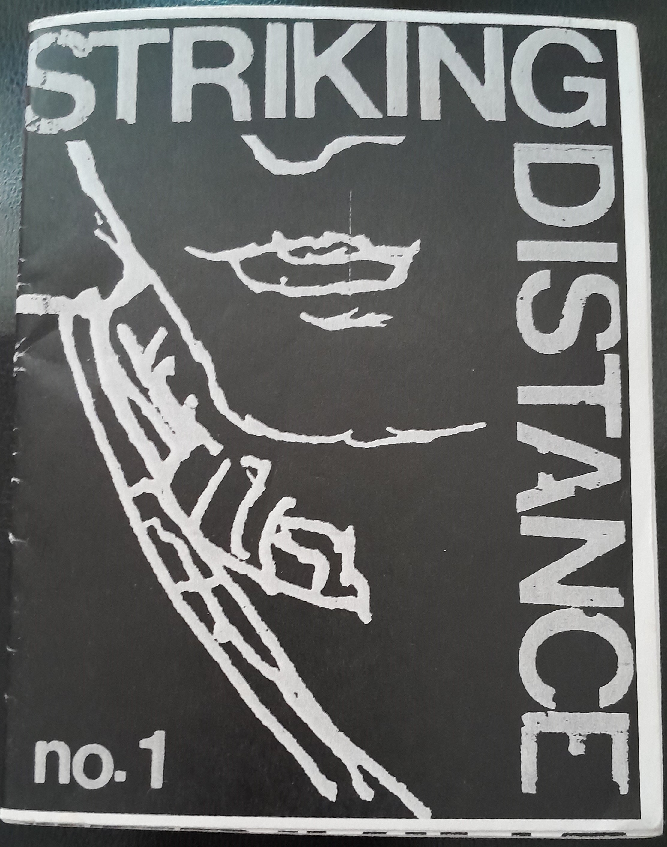 A black cover with the title, "Striking Distance" written across the top and right edges of the cover in gray letters in a reverse L shape. The cover depicts a close-up of a person, drawn exclusively in gray outlines, cropped so that you can only see from the nose down to the bottom of the collar of their shirt, and the outline of their shoulder stretching to the edge of the page. "No. 1", shorthand for Number 1, is written in the bottom left hand corner.