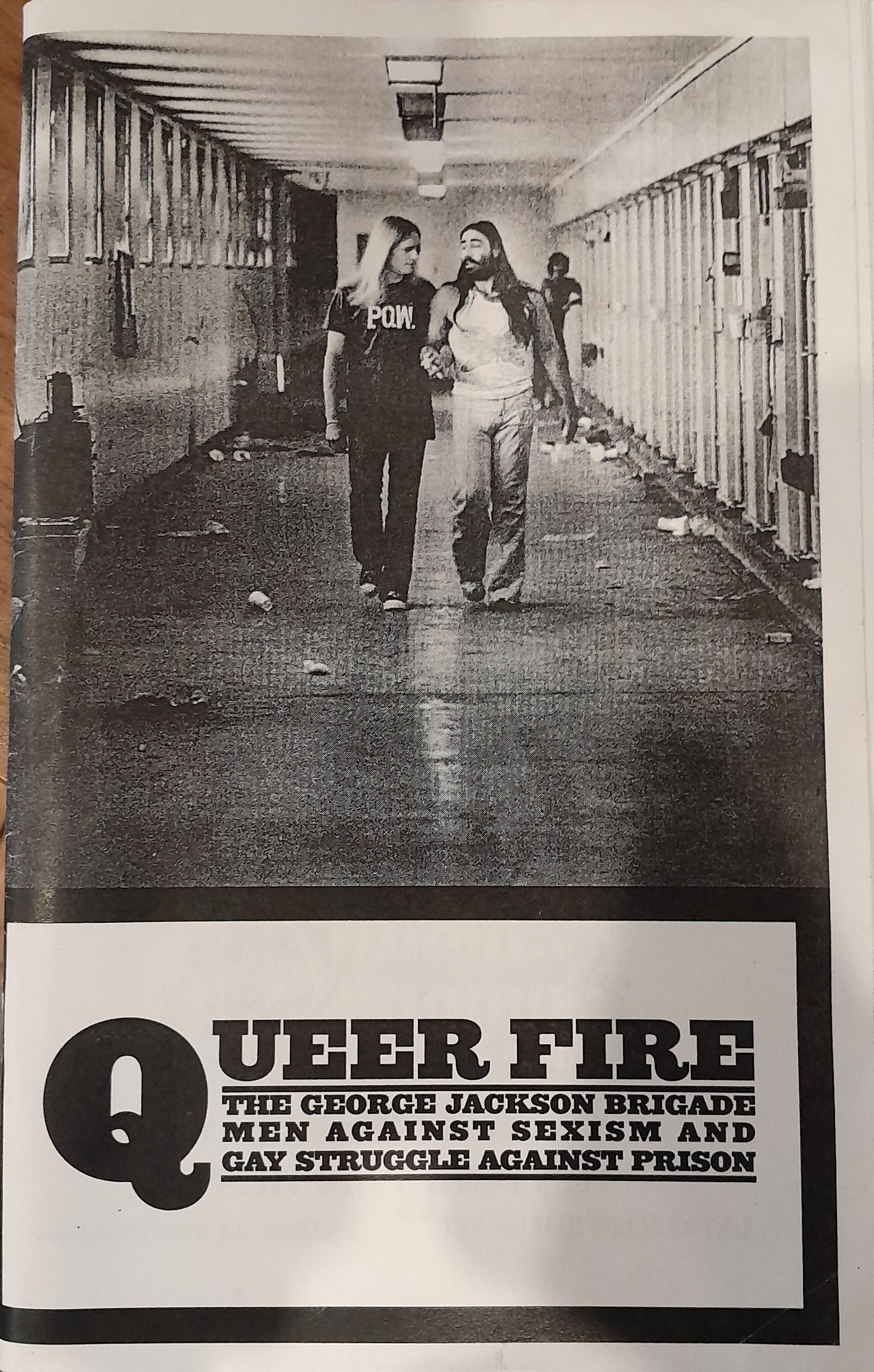 A black and white photograph depicting two individuals with long hair- Danny Atteberry and co-author Ed Mead- walking hand in hand through the halls of a prison cell block in the midst of a conversation.