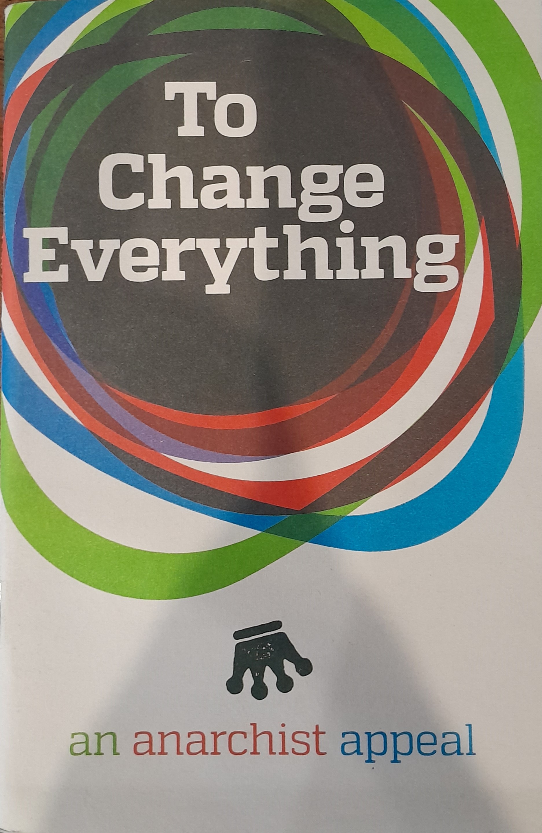 The front cover depicts the title text, "To Change Everything" inside of a series of interlocking circles of several different colours. Below this imagery of interlocking circles is an upside down crown, and below that the subtitle, "an anarchist appeal", is written in green, red, and blue text.
