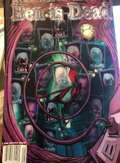 What looks like a purple tree hole frames the cover art and has an electrical cord plugged into it, also purple. This chord spirals and the other end is attatched to the head of a red humanoid creature which is suspended in the centre of the zine. The background has little turquoise creatures holding up framed headshots that are purple or turquoise.