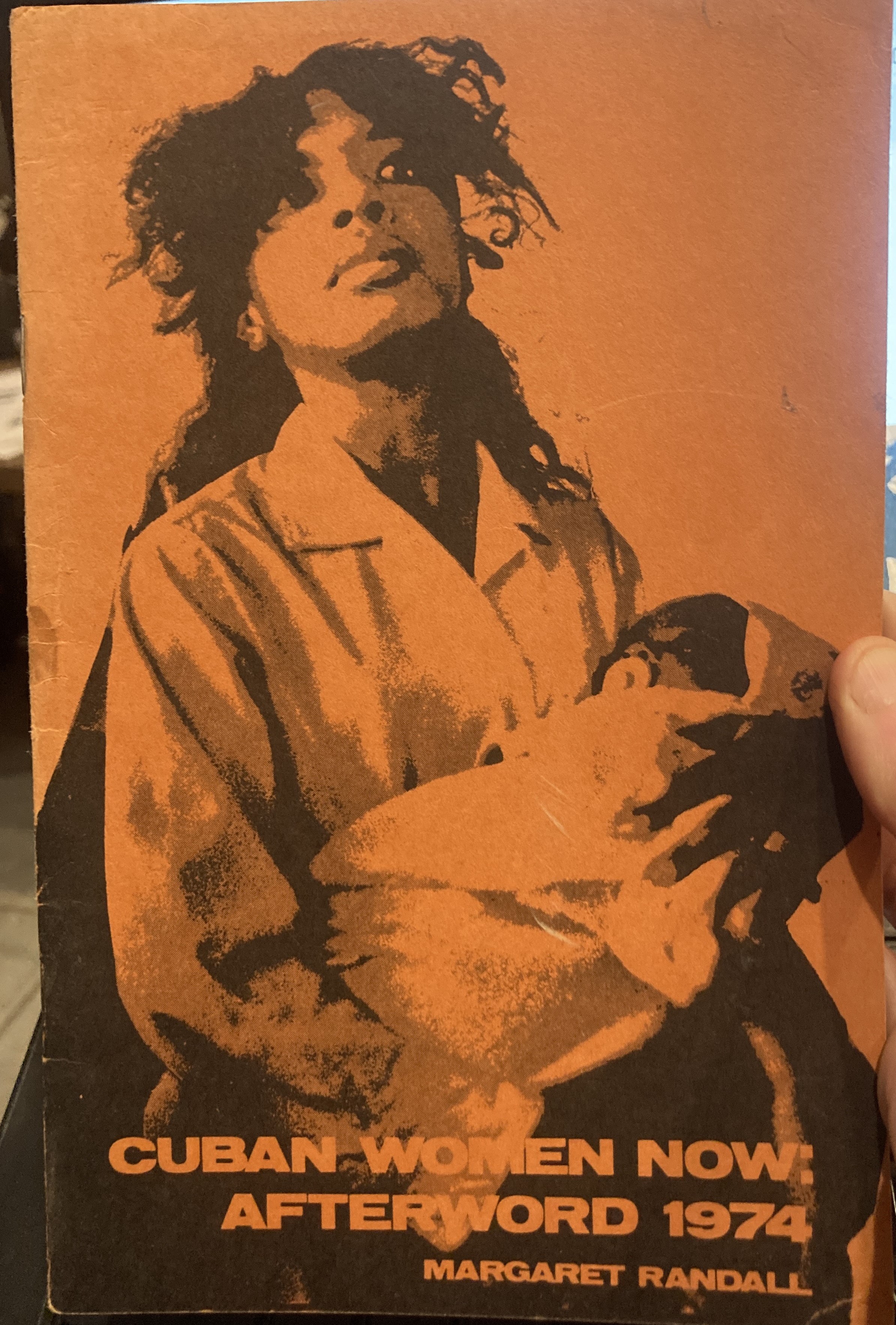 Cover of the zine "Cuban Women Now," with an orange and black print of a person with long curly hair holding a baby
