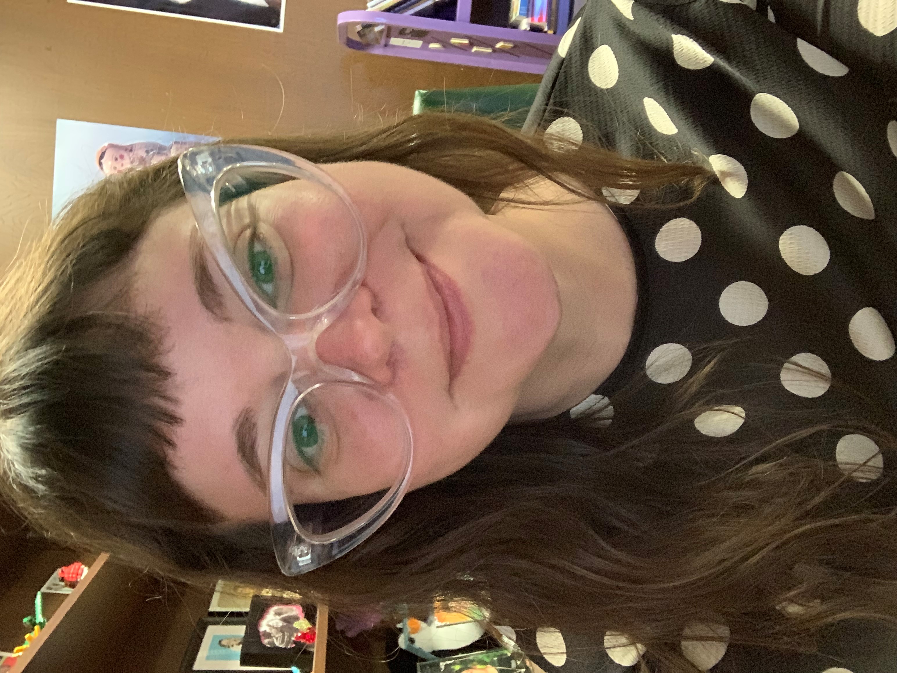 Photograph of a smiling person with brown hair and a black and white polka dot shirt